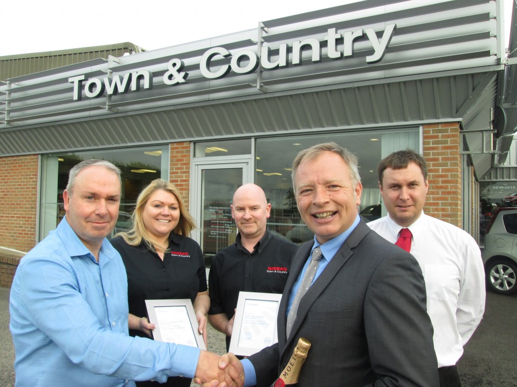Mick Wheeler, Sales Executive at Town and Country Nissan, receives a bottle of champagne from Steven Murr, Motability Dealer Development Manager. Back row, from left, are Town and Country staff members Marcus Lean, Natalie Bunt and Mat Hedger